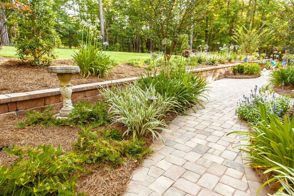 Diseño de jardín clásico en patio trasero con jardín francés, muro de contención y adoquines de ladrillo