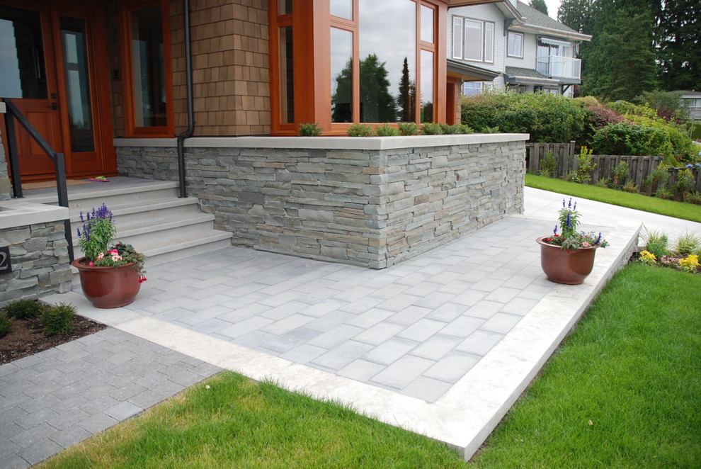 Photo of a large contemporary front driveway full sun garden in Vancouver with a retaining wall and natural stone paving.