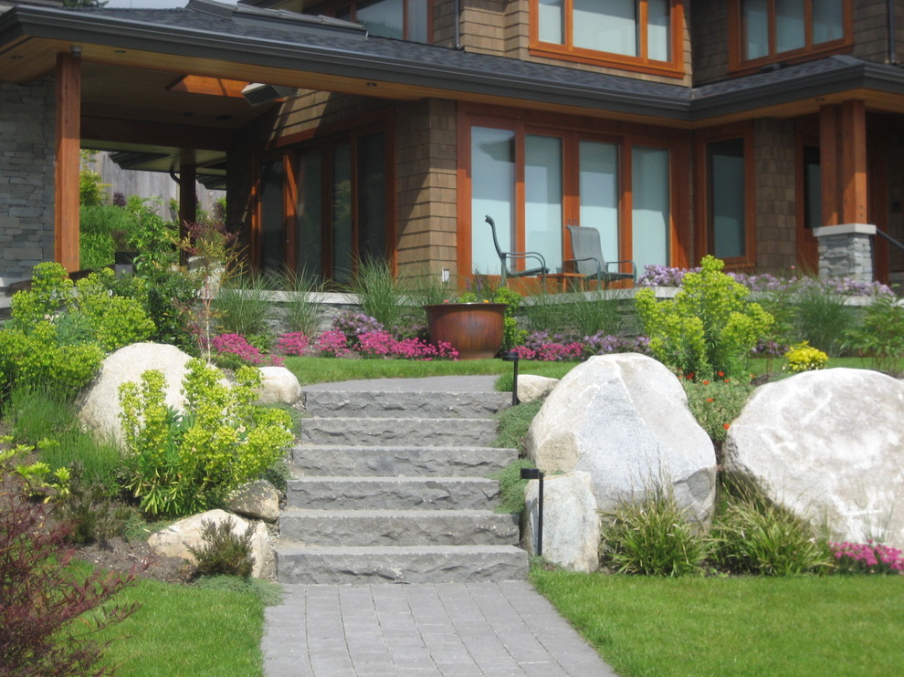 Large contemporary front driveway full sun garden in Vancouver with a retaining wall and natural stone paving.