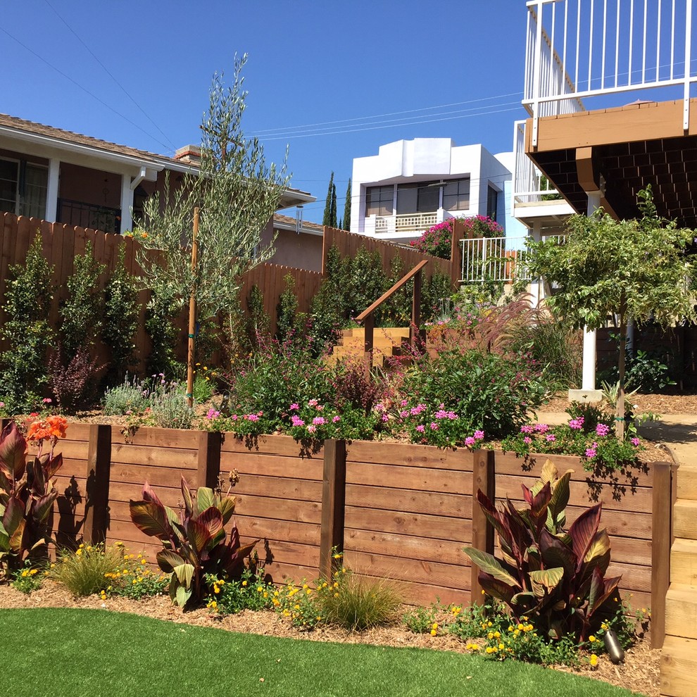 Свежая идея для дизайна: большой солнечный, летний регулярный сад на переднем дворе в средиземноморском стиле с подпорной стенкой, хорошей освещенностью, настилом и с деревянным забором - отличное фото интерьера