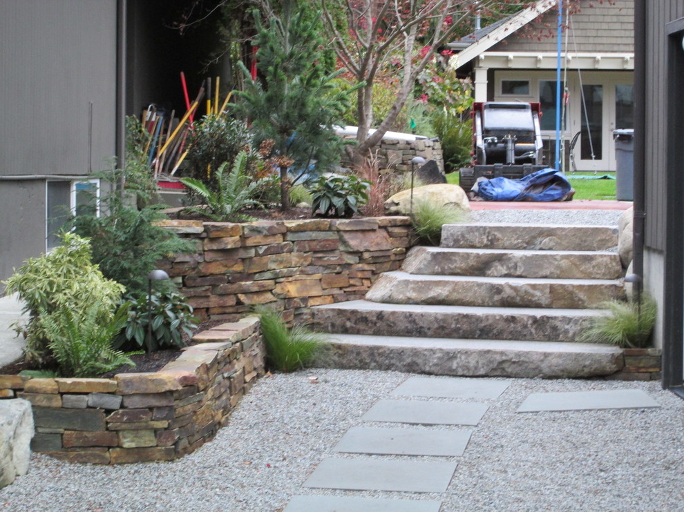 This is an example of a large coastal partial sun side yard stone retaining wall landscape in Seattle.