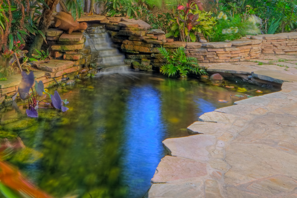 Foto di un grande laghetto da giardino tropicale in ombra dietro casa con pavimentazioni in pietra naturale