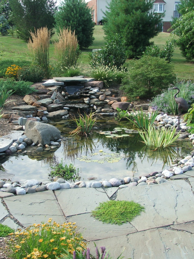 This is an example of a traditional full sun backyard concrete paver water fountain landscape in DC Metro.
