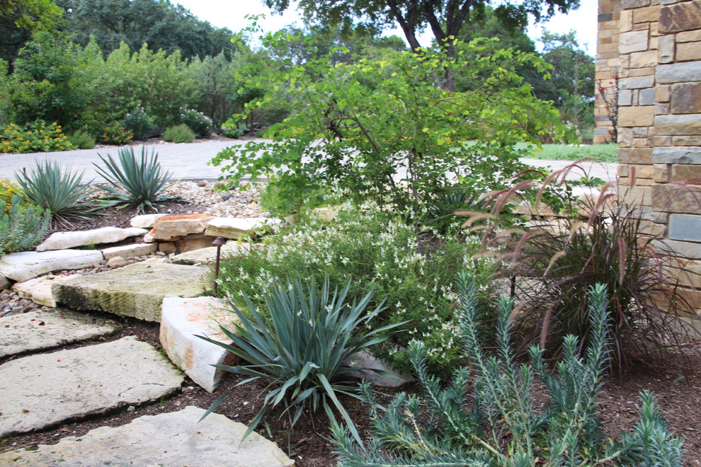 Photo of a large classic side xeriscape partial sun garden in Austin with natural stone paving.