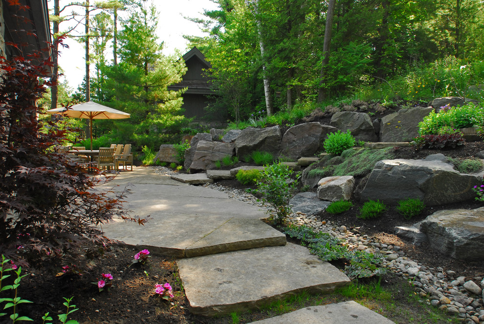Aménagement d'un très grand jardin arrière montagne au printemps avec un mur de soutènement, une exposition ensoleillée et des pavés en pierre naturelle.