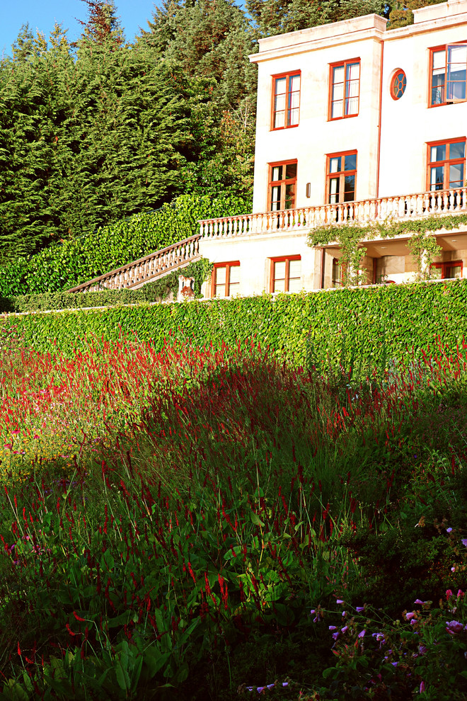 Cette image montre un grand jardin à la française arrière traditionnel au printemps avec une exposition ensoleillée et du gravier.