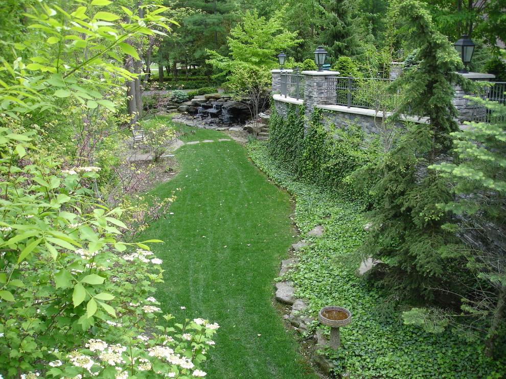 Immagine di un grande giardino tradizionale esposto a mezz'ombra davanti casa in estate con un muro di contenimento e pavimentazioni in pietra naturale