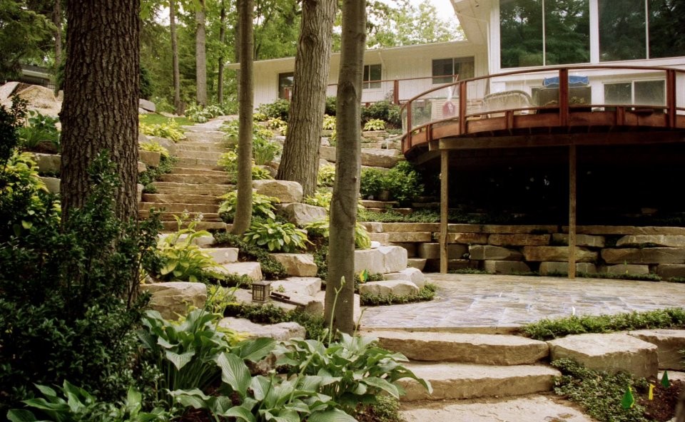 Immagine di un ampio giardino moderno in ombra in estate con pavimentazioni in pietra naturale, un pendio, una collina o una riva e un muro di contenimento