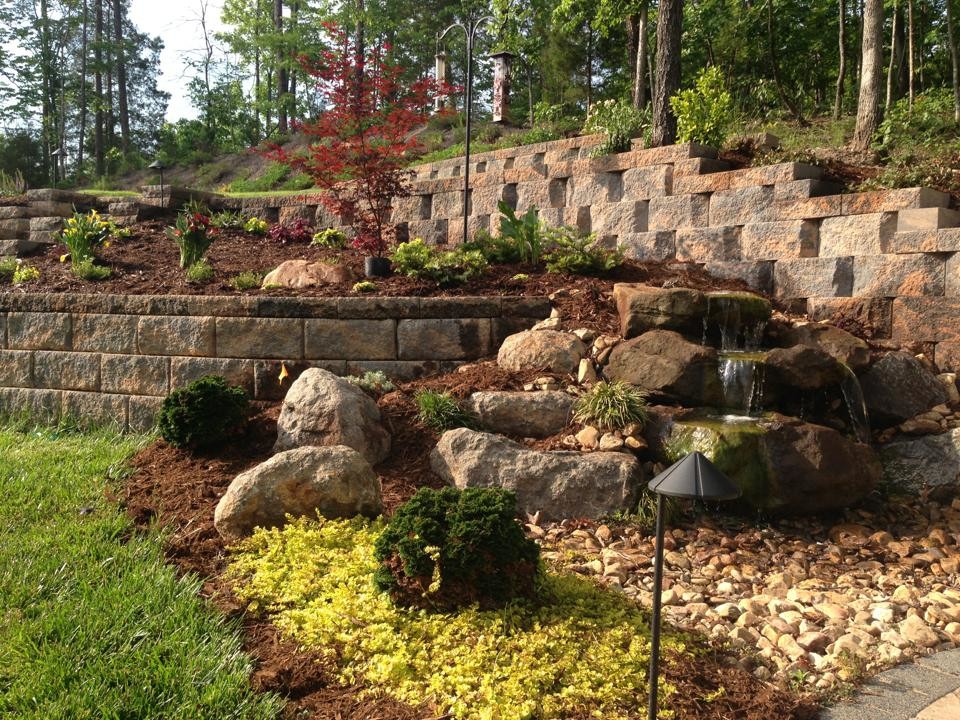 This is an example of a traditional full sun backyard mulch retaining wall landscape in Charlotte for summer.