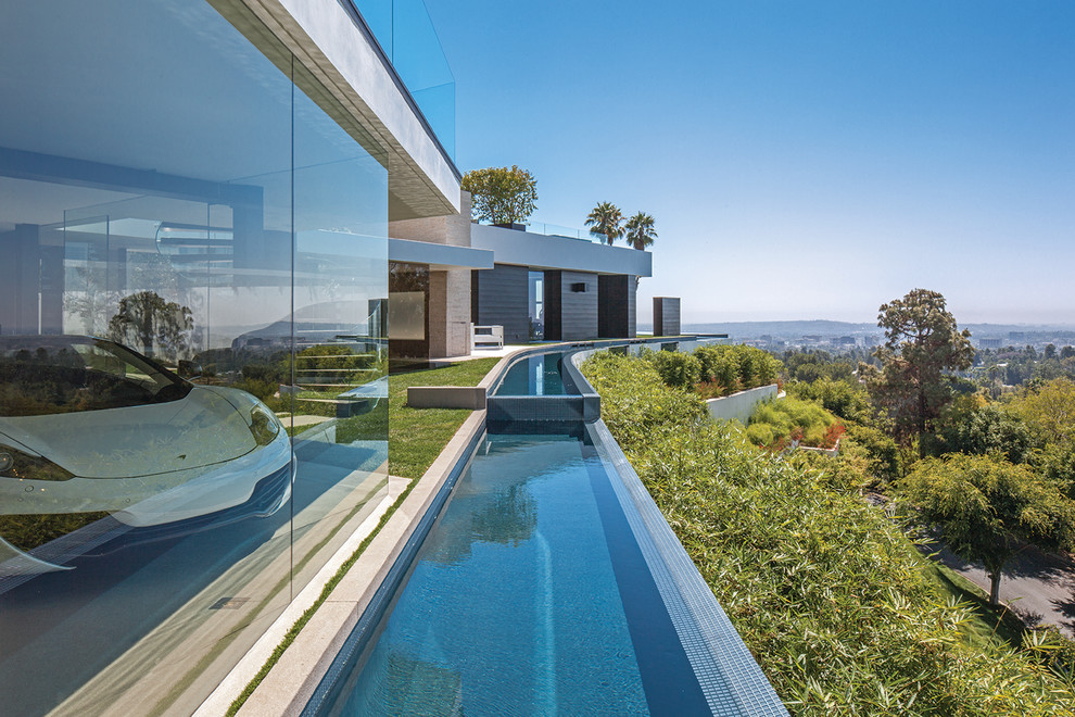 Imagen de piscina infinita moderna extra grande a medida en patio lateral con paisajismo de piscina y suelo de baldosas