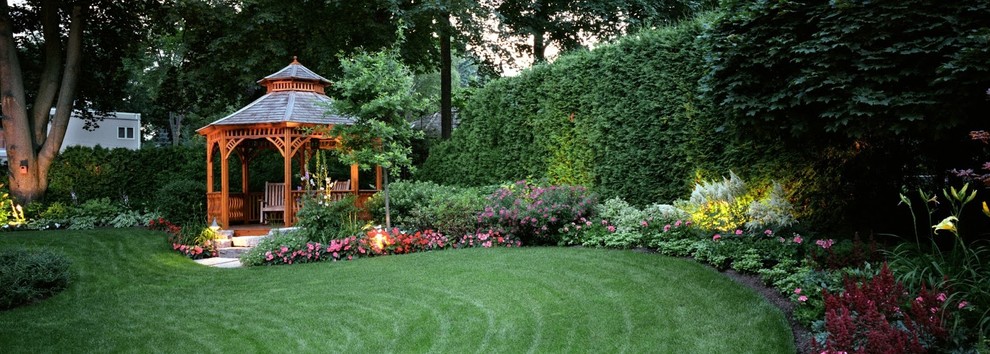 Exempel på en stor klassisk trädgård i delvis sol på sommaren, med utekrukor och trädäck