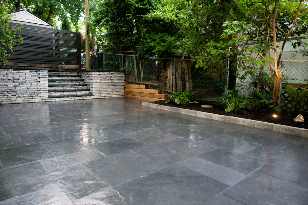 This is an example of a large modern back formal partial sun garden for spring in Toronto with a retaining wall and natural stone paving.