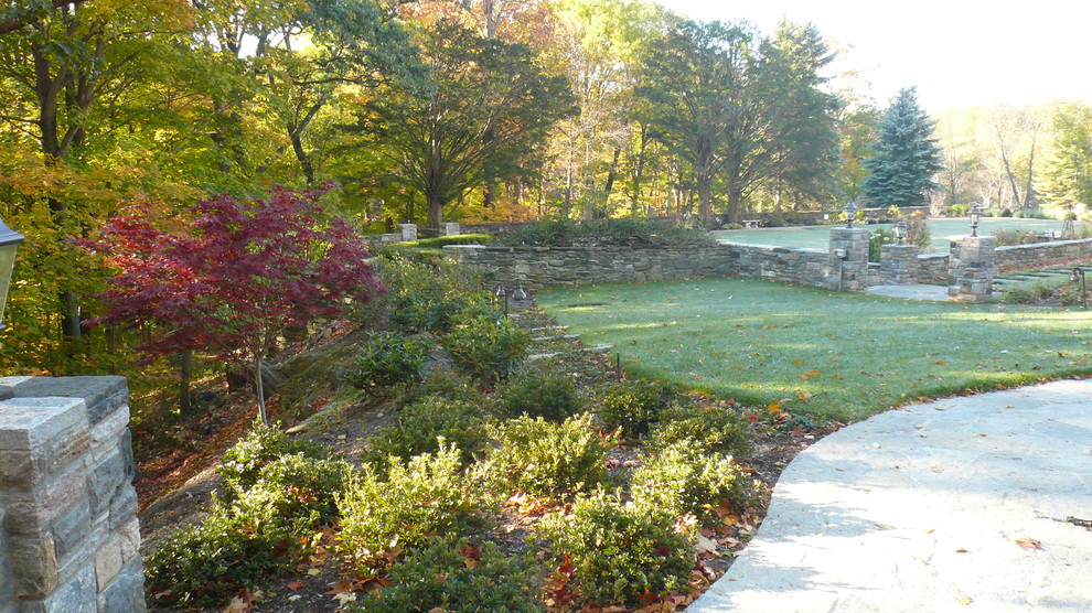 Immagine di un ampio giardino formale tradizionale esposto in pieno sole dietro casa in estate con pavimentazioni in pietra naturale e un muro di contenimento