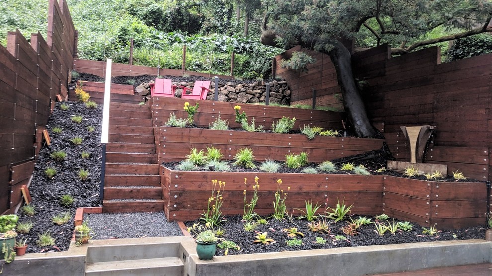 На фото: солнечный засухоустойчивый сад среднего размера на заднем дворе в средиземноморском стиле с подпорной стенкой, мульчированием, хорошей освещенностью и с деревянным забором с