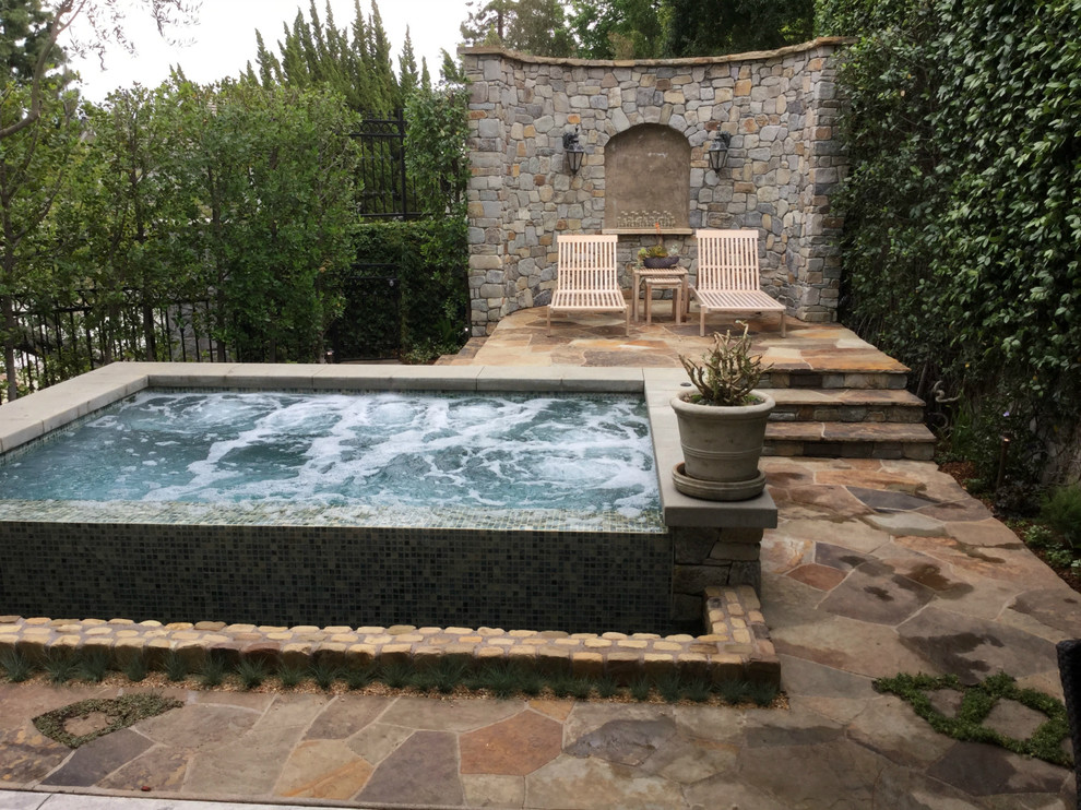 This is an example of a large eclectic back partial sun garden in Los Angeles with a water feature and natural stone paving.