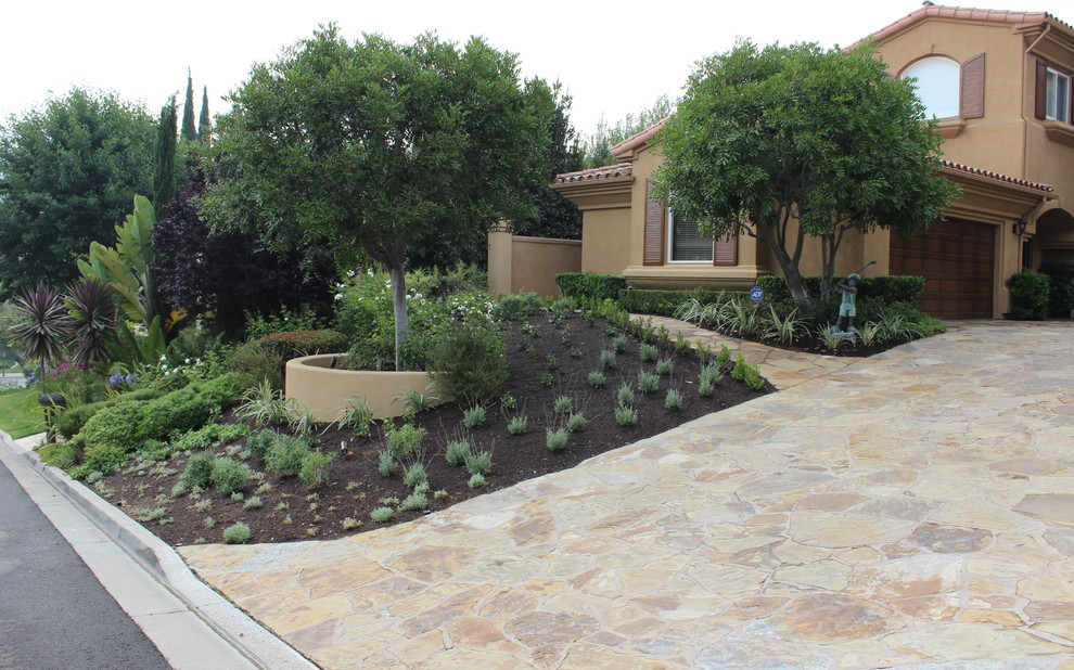 Mittelgroßer Mediterraner Vorgarten mit Feuerstelle, Auffahrt, direkter Sonneneinstrahlung und Natursteinplatten in Orange County
