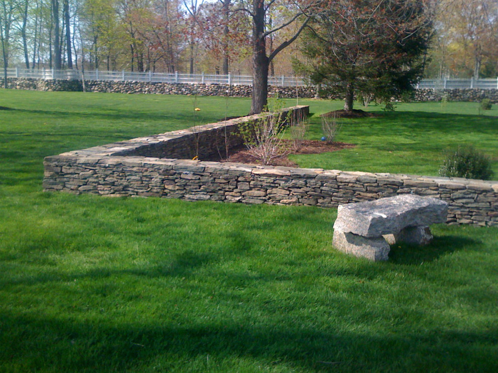 Large traditional back partial sun garden in New York with a retaining wall and mulch.