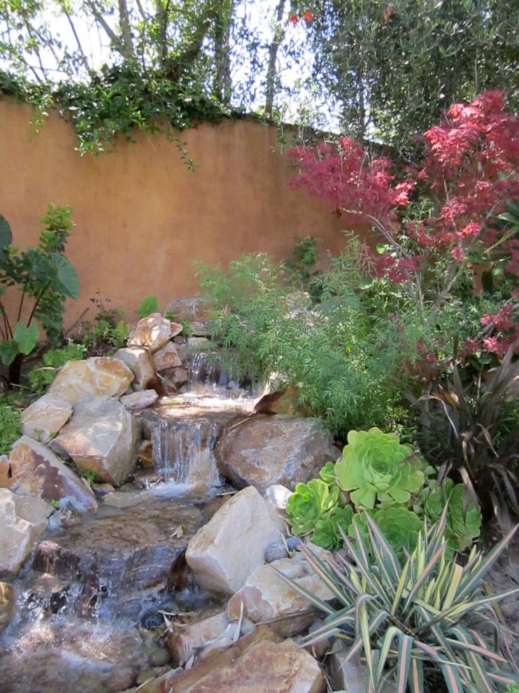 Großer Mediterraner Garten im Sommer, hinter dem Haus mit direkter Sonneneinstrahlung, Natursteinplatten und Wasserspiel in Los Angeles
