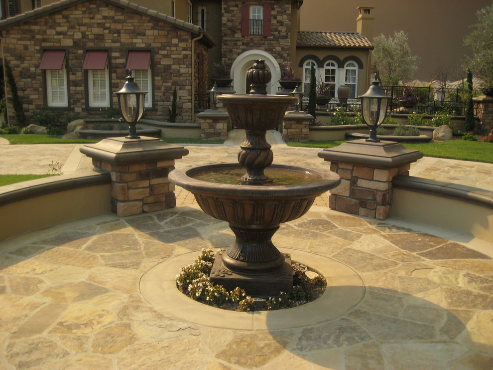 Immagine di un grande giardino mediterraneo esposto in pieno sole davanti casa con fontane e pavimentazioni in pietra naturale