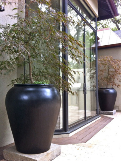 На фото: большой весенний регулярный сад на внутреннем дворе в стиле неоклассика (современная классика) с растениями в контейнерах, покрытием из каменной брусчатки и полуденной тенью