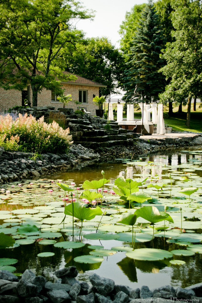 Aménagement d'un grand jardin arrière classique au printemps avec un point d'eau, une exposition partiellement ombragée et des pavés en pierre naturelle.