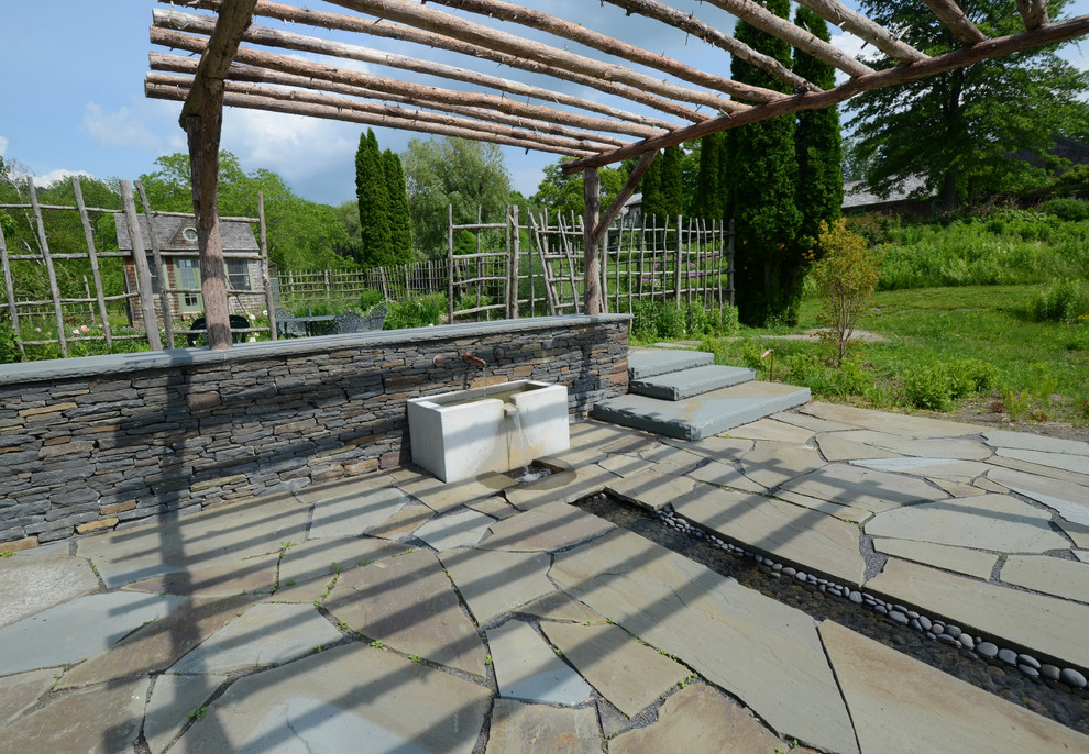 Expansive rustic back formal full sun garden for summer in New York with a water feature and natural stone paving.