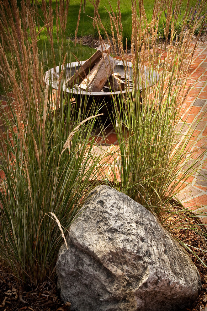 Modelo de jardín bohemio de tamaño medio en verano en patio trasero con brasero, exposición total al sol y adoquines de ladrillo