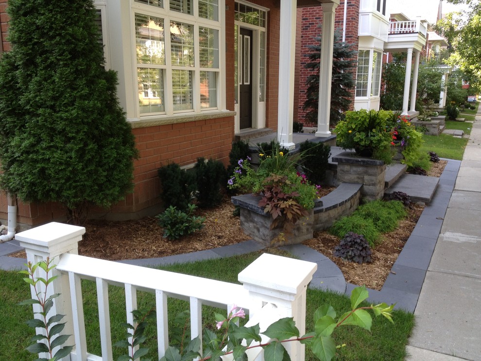 Photo of a small contemporary front driveway fully shaded garden for autumn in Toronto with a retaining wall and natural stone paving.