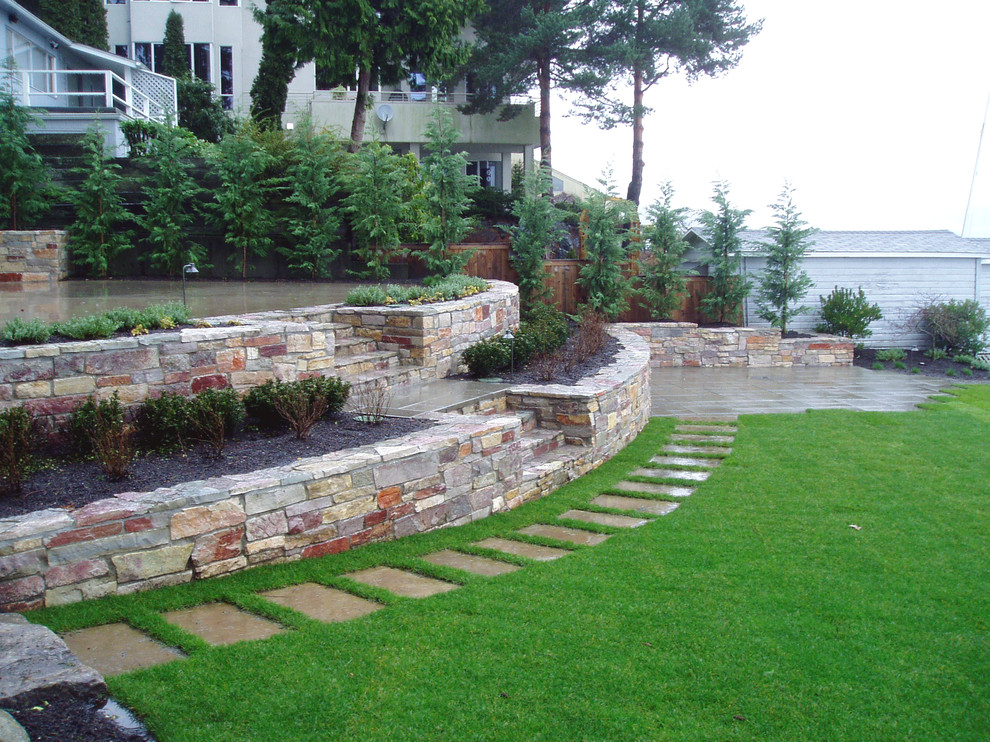 This is an example of a large classic back formal full sun garden for spring in Seattle with a retaining wall and natural stone paving.
