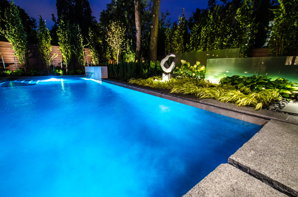 This is an example of a small contemporary back swimming pool in Toronto with a water feature and natural stone paving.