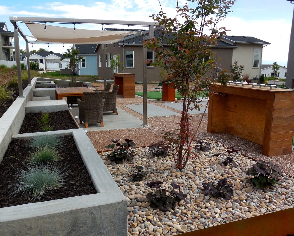 На фото: солнечный засухоустойчивый сад среднего размера на заднем дворе в современном стиле с хорошей освещенностью, покрытием из гравия и подпорной стенкой с