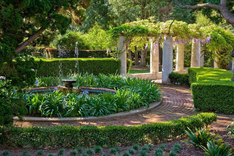 Inspiration för medelhavsstil formella trädgårdar i delvis sol på våren, med en fontän och marksten i tegel