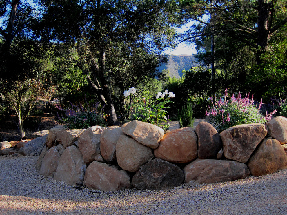 Inspiration for a medium sized mediterranean front xeriscape partial sun garden for summer in Santa Barbara with gravel and a retaining wall.