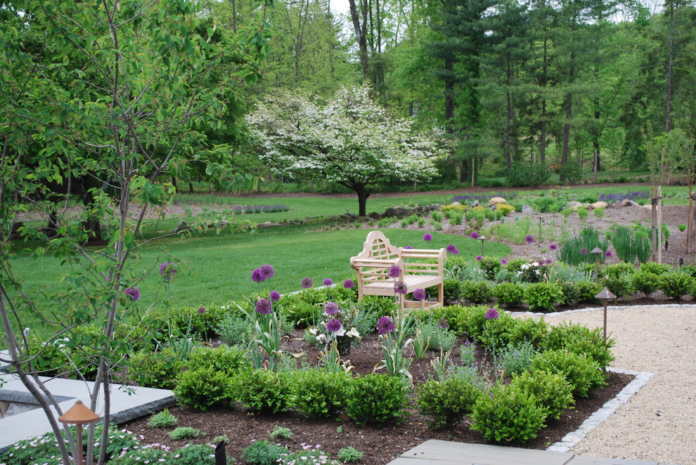 Exempel på en stor klassisk trädgård i full sol på våren, med grus