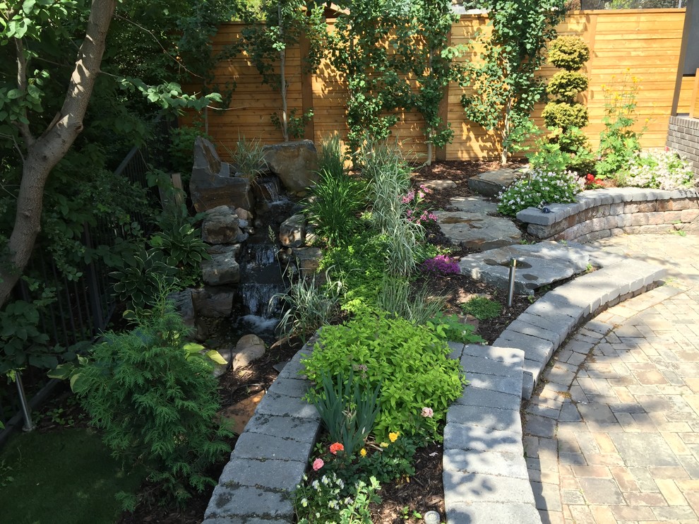 Small traditional back full sun garden for summer in Calgary with a water feature and natural stone paving.