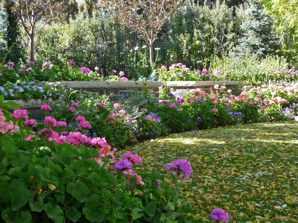 Exempel på en klassisk trädgård framför huset, med en stödmur och naturstensplattor