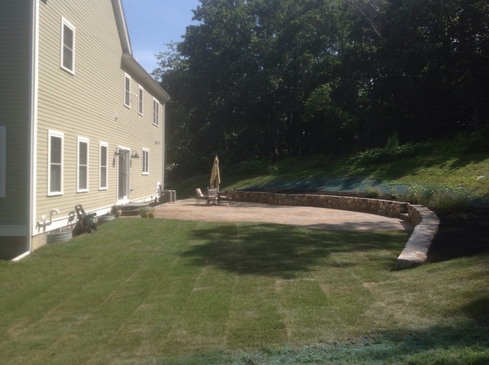 Large classic back garden in Boston with a retaining wall and concrete paving.
