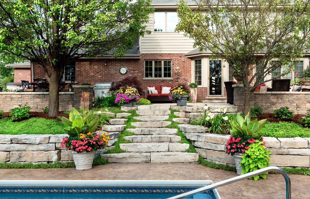 Ejemplo de jardín tradicional renovado de tamaño medio en verano en patio trasero con muro de contención, exposición total al sol y adoquines de piedra natural