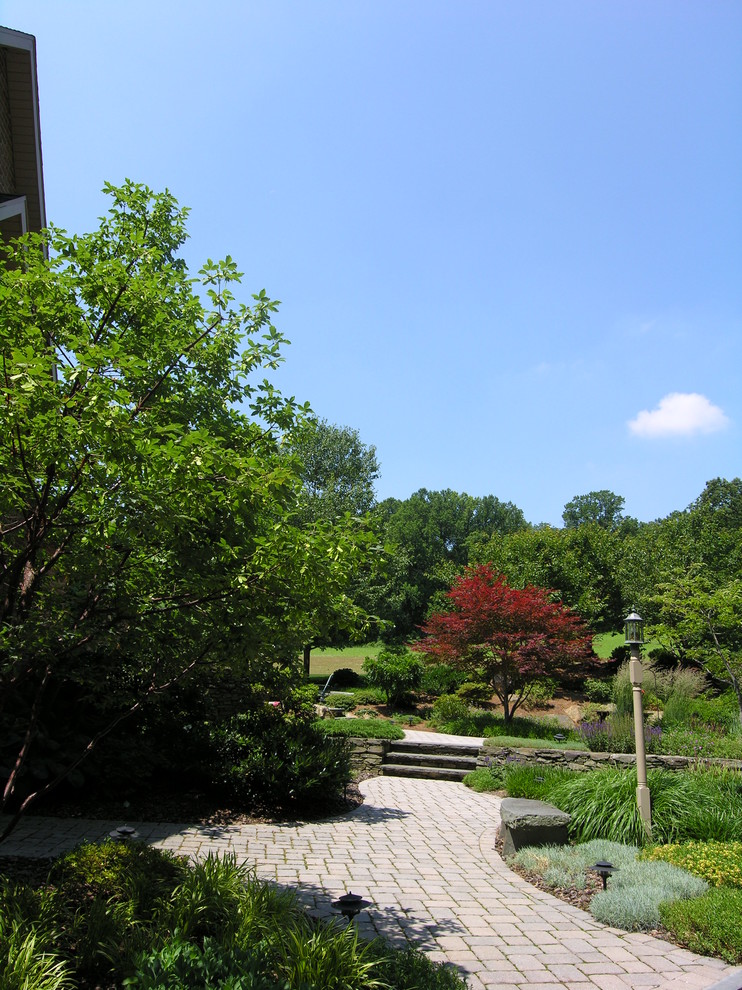 Imagen de jardín clásico renovado grande en verano en patio trasero con muro de contención, exposición total al sol y adoquines de ladrillo