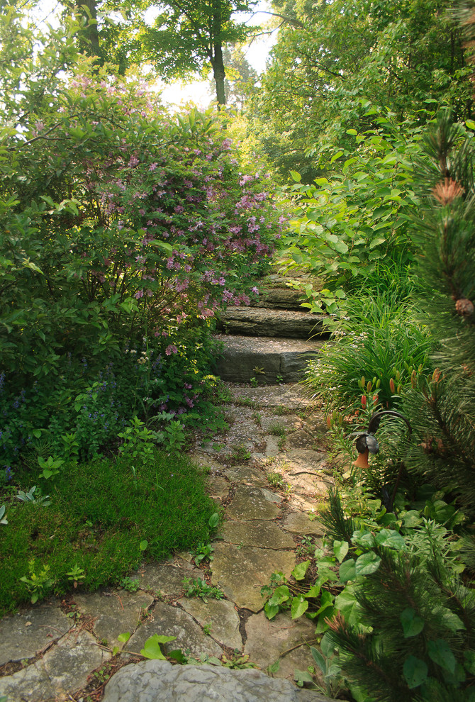 Réalisation d'un très grand jardin arrière tradition l'été avec un mur de soutènement, une exposition partiellement ombragée et des pavés en pierre naturelle.