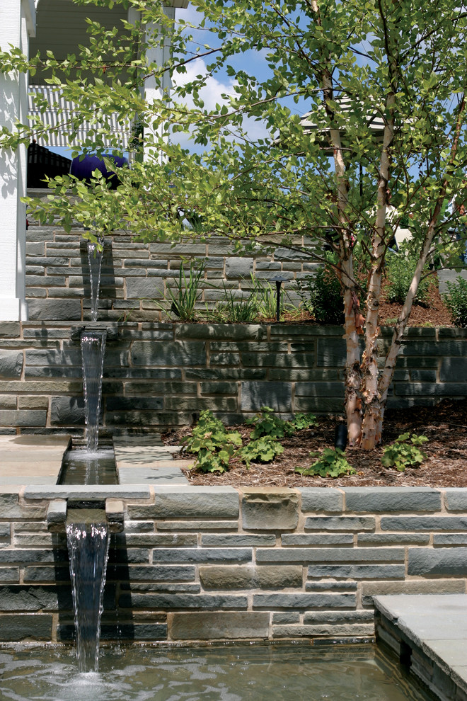 This is an example of a modern back garden in Chicago with a water feature and natural stone paving.