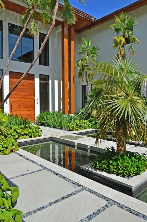 Стильный дизайн: большой солнечный участок и сад на переднем дворе в восточном стиле с подъездной дорогой, хорошей освещенностью и покрытием из каменной брусчатки - последний тренд