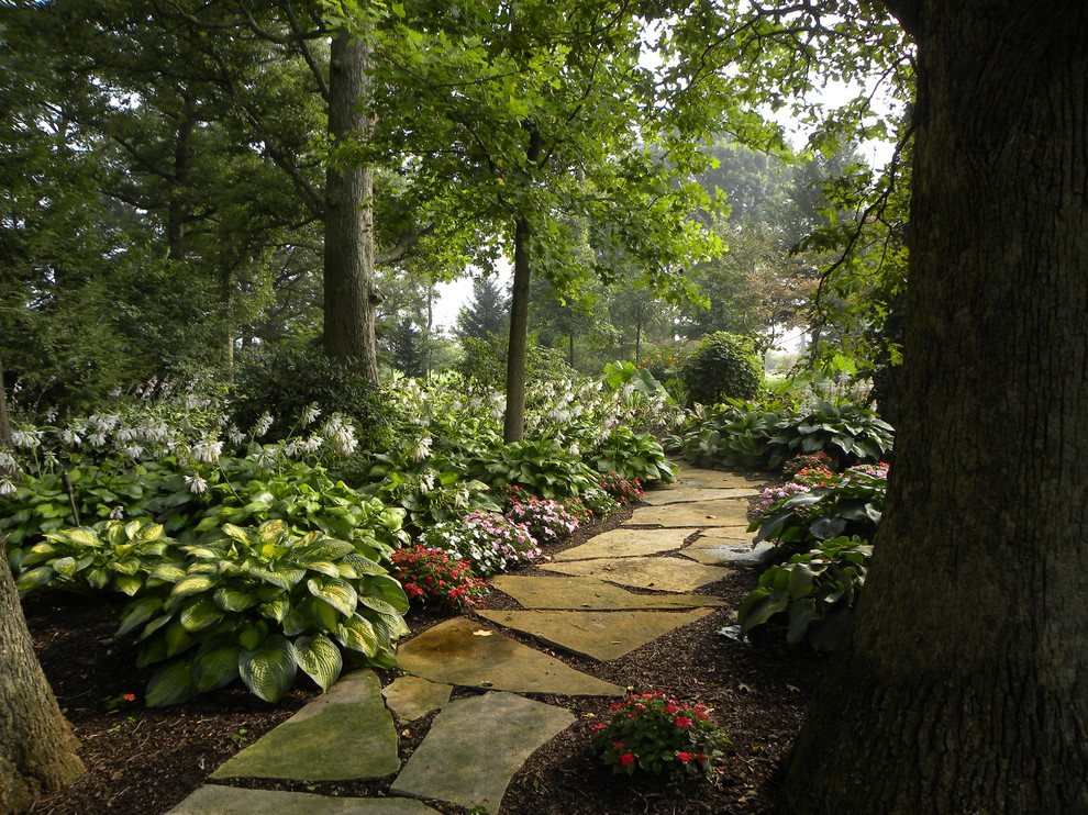 Aménagement d'un grand jardin latéral contemporain l'été avec une exposition ombragée et des pavés en pierre naturelle.