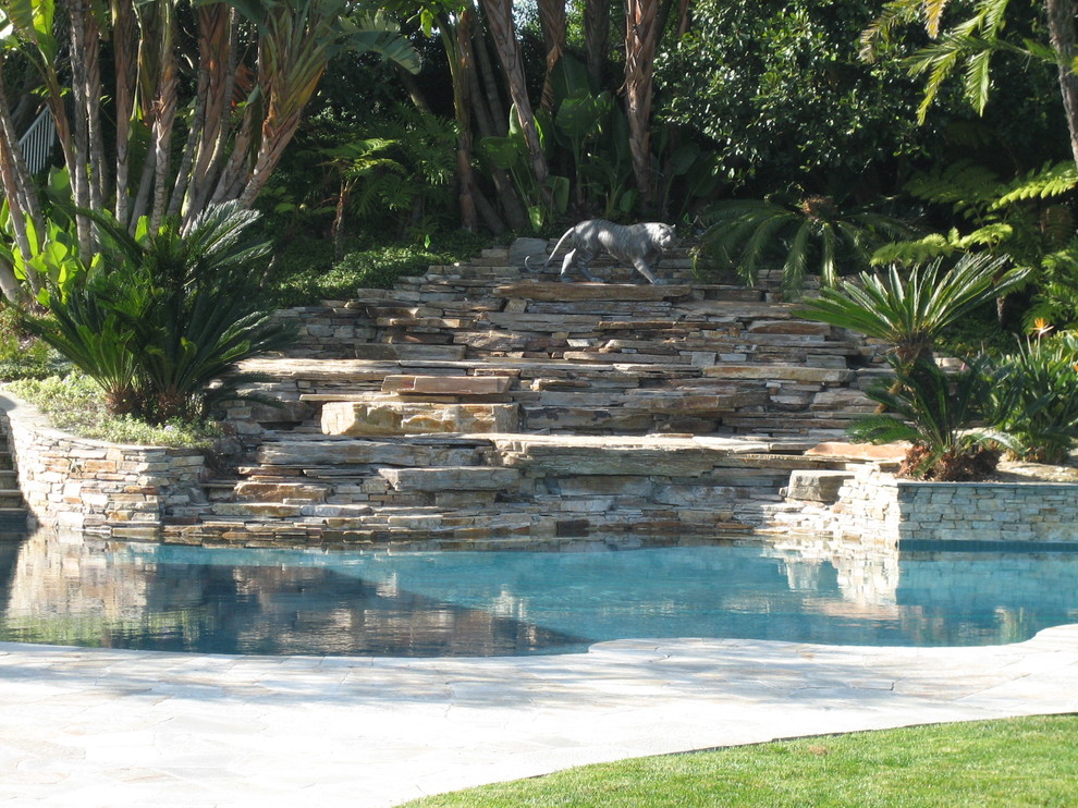 Modelo de jardín tropical extra grande en patio trasero con muro de contención, exposición parcial al sol y adoquines de piedra natural