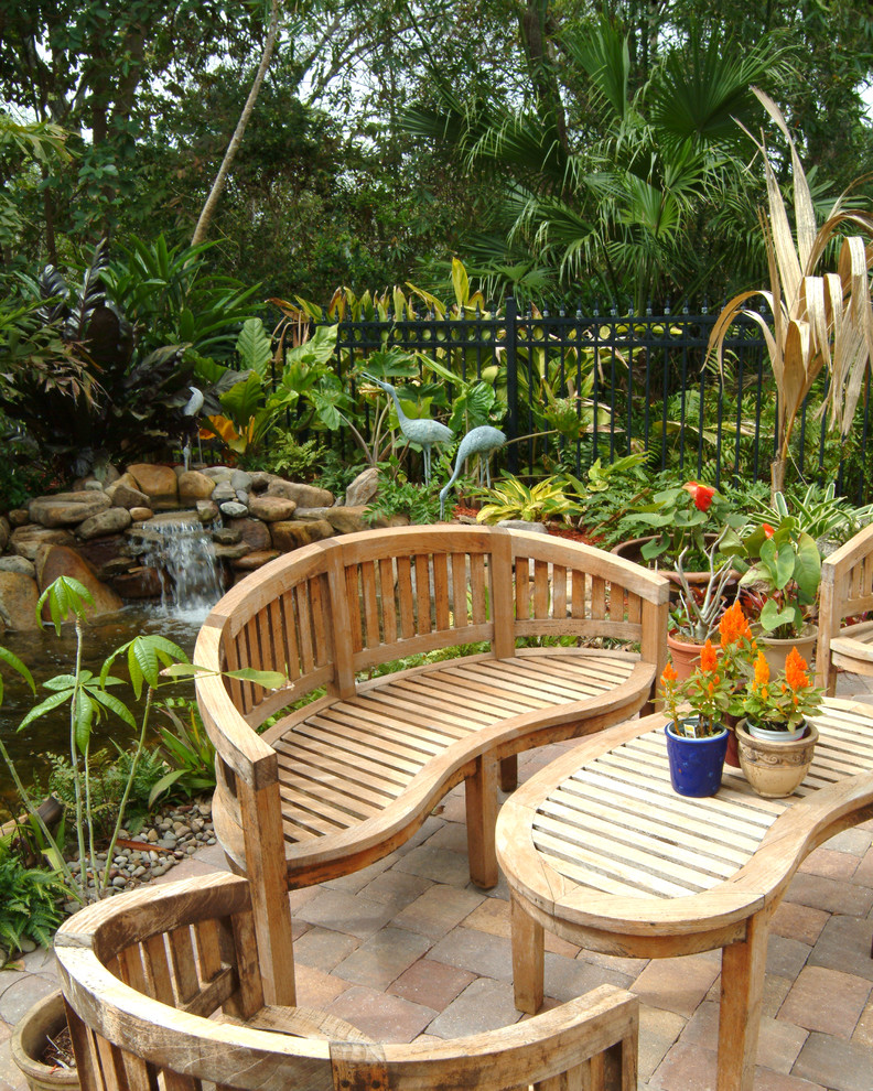 Ejemplo de jardín ecléctico con adoquines de ladrillo y fuente