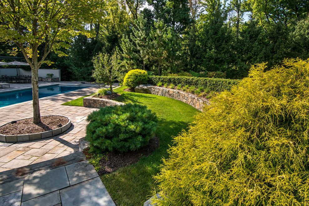 Large classic back partial sun garden for autumn in New York with a retaining wall and natural stone paving.