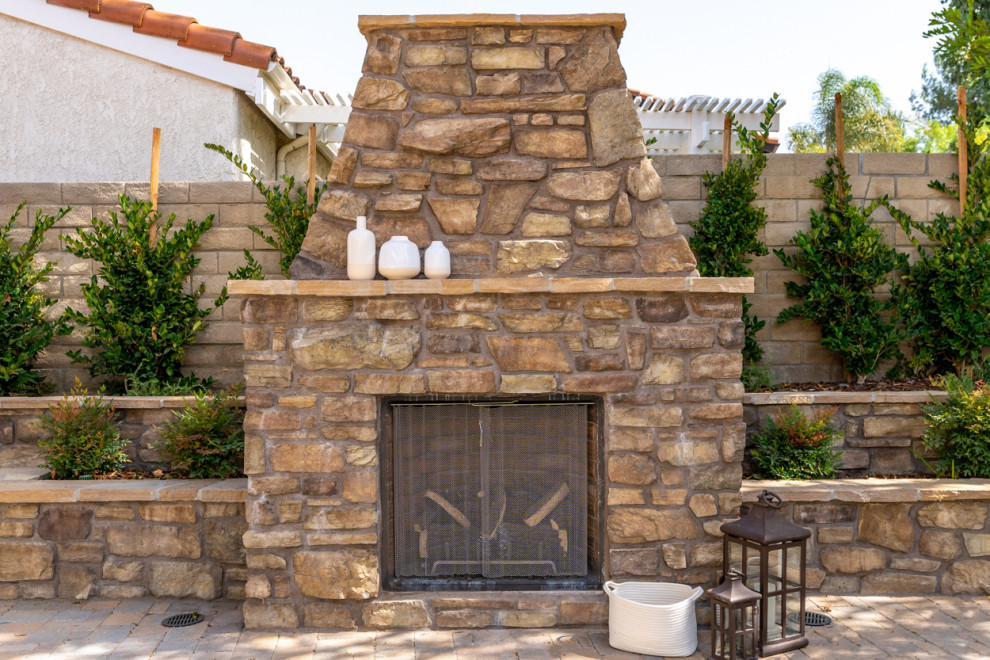 Geräumiger Mediterraner Patio hinter dem Haus mit Kamin und Natursteinplatten in Los Angeles