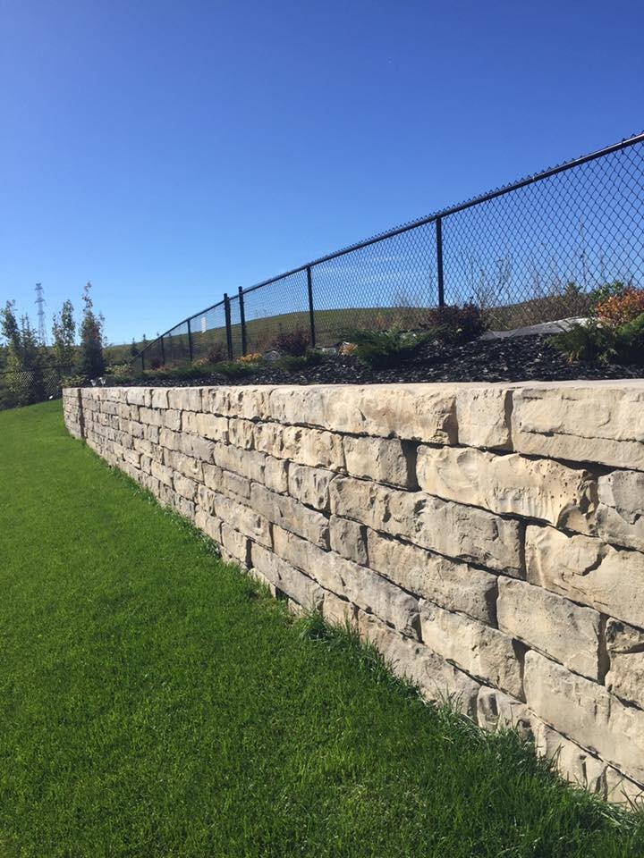 This is an example of a large traditional side full sun garden in Calgary with a retaining wall and natural stone paving.