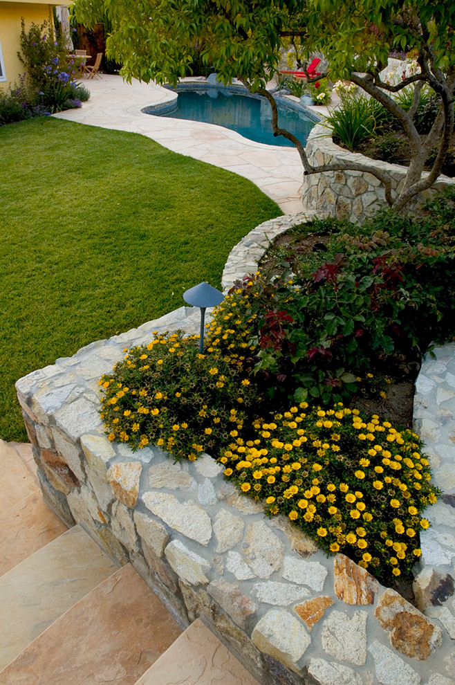 Esempio di un grande giardino mediterraneo esposto a mezz'ombra dietro casa in estate con un muro di contenimento e pavimentazioni in pietra naturale