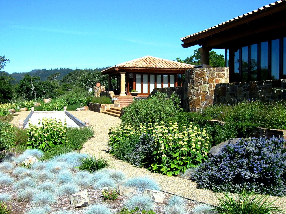 Diseño de jardín de secano mediterráneo en patio trasero con fuente, exposición total al sol y gravilla